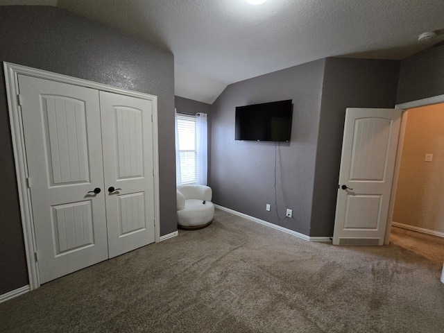 unfurnished bedroom featuring baseboards, lofted ceiling, a closet, a textured ceiling, and carpet flooring