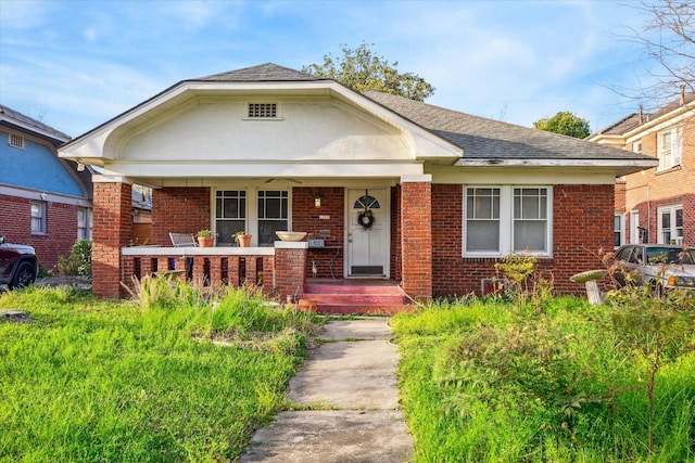 bungalow featuring brick siding, covered porch, and roof with shingles