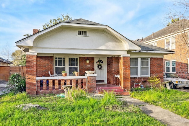 view of front of home with stucco siding, brick siding, a porch, and a chimney