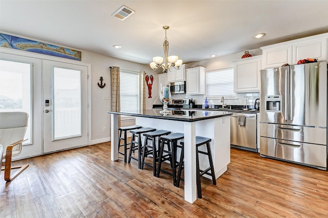 kitchen featuring visible vents, a kitchen island, a breakfast bar, appliances with stainless steel finishes, and dark countertops