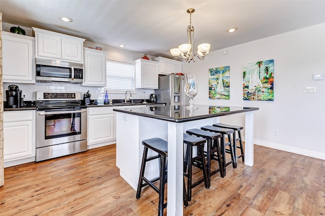 kitchen featuring a breakfast bar, appliances with stainless steel finishes, dark countertops, tasteful backsplash, and a chandelier