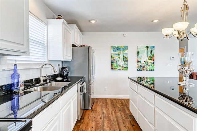 kitchen featuring a notable chandelier, a sink, dark countertops, wood finished floors, and white cabinetry