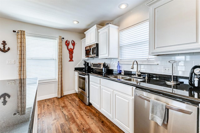 kitchen with dark countertops, backsplash, light wood-type flooring, stainless steel appliances, and a sink