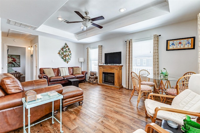 living room featuring a ceiling fan, visible vents, a tray ceiling, attic access, and light wood-type flooring