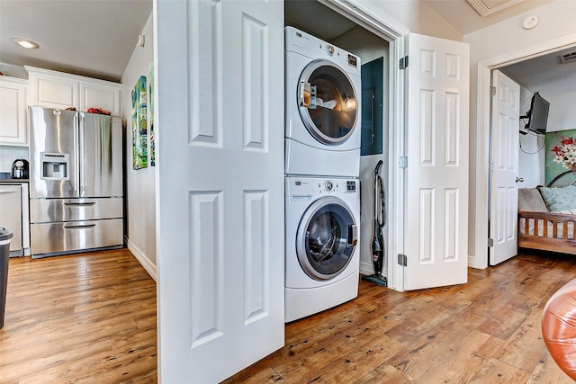 washroom with visible vents, light wood-style flooring, stacked washing maching and dryer, baseboards, and laundry area