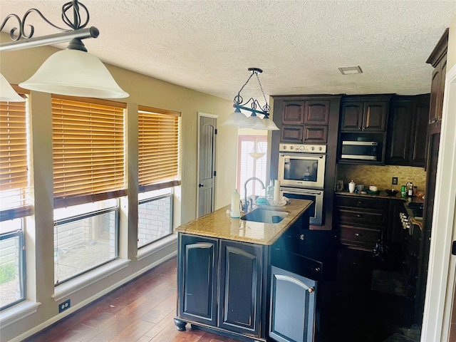 kitchen featuring black microwave, dark wood finished floors, decorative light fixtures, stainless steel double oven, and a sink