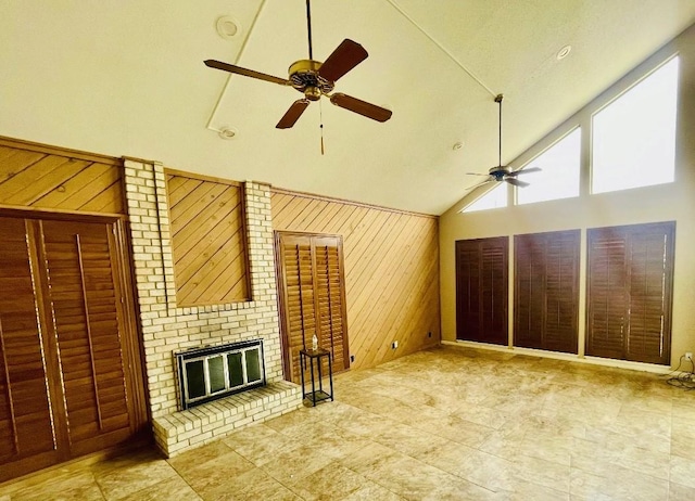 unfurnished living room featuring high vaulted ceiling, a fireplace, wood walls, and ceiling fan