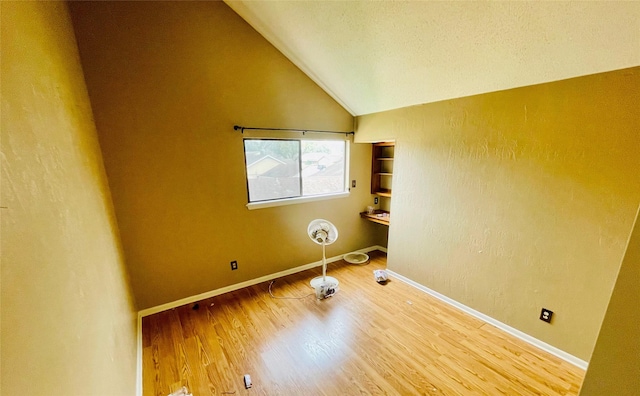 unfurnished room with a textured ceiling, wood finished floors, baseboards, vaulted ceiling, and a textured wall