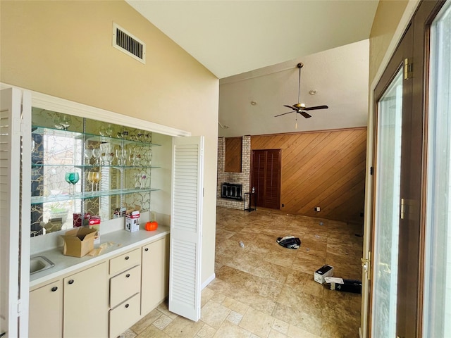 interior space featuring visible vents, a brick fireplace, ceiling fan, wood walls, and vaulted ceiling