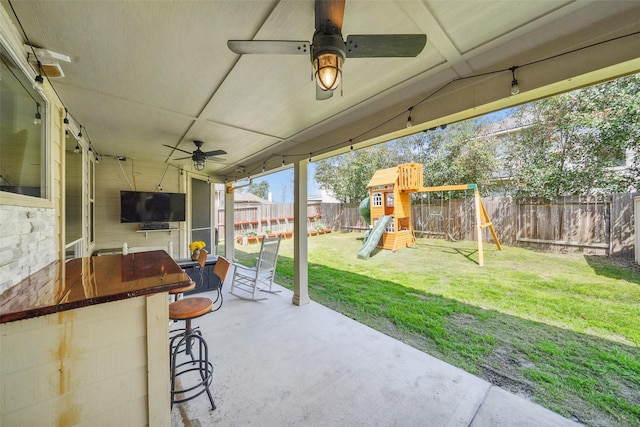 view of patio / terrace featuring a ceiling fan, a playground, a fenced backyard, and outdoor dry bar