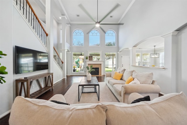 living area with wood finished floors, baseboards, ornate columns, arched walkways, and crown molding