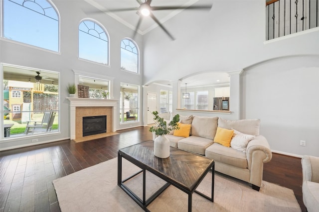 living area with baseboards, wood finished floors, ceiling fan, and ornate columns