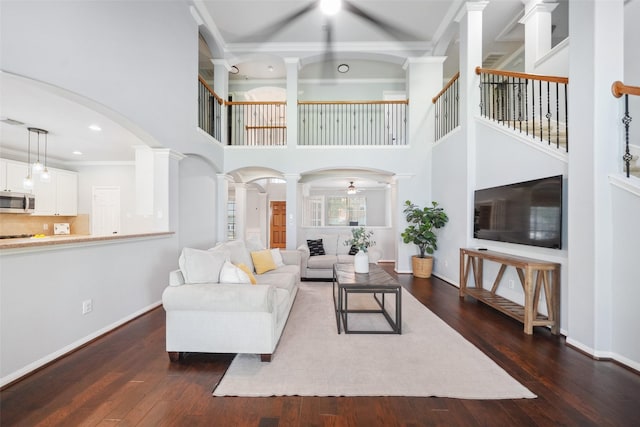 living room featuring dark wood-style floors, arched walkways, baseboards, ceiling fan, and ornate columns