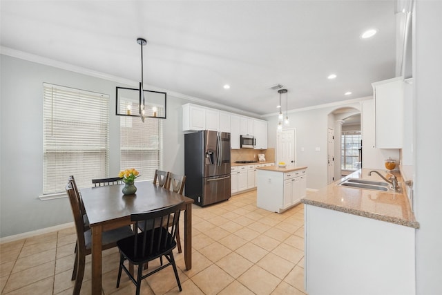 interior space with a kitchen island, arched walkways, a sink, appliances with stainless steel finishes, and crown molding