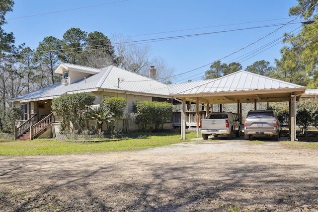 view of side of home featuring a detached carport, a lawn, a chimney, metal roof, and driveway