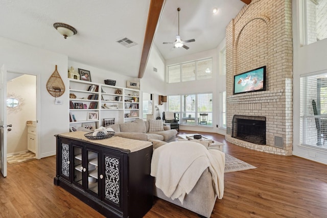 living room with a brick fireplace, wood finished floors, visible vents, and ceiling fan