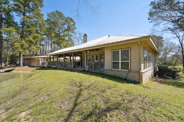 rear view of property with a yard, covered porch, metal roof, brick siding, and a chimney