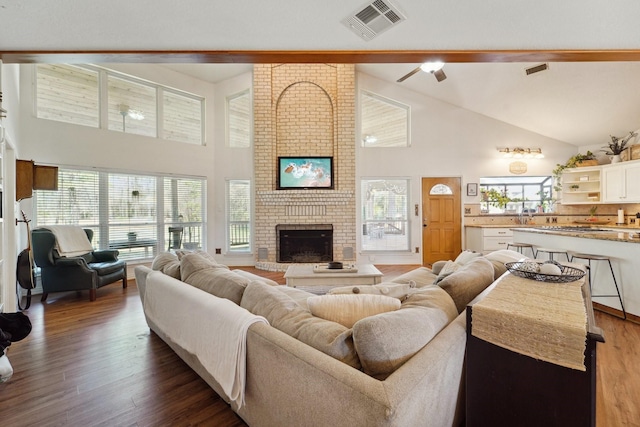 living room featuring visible vents, a fireplace, high vaulted ceiling, and wood finished floors