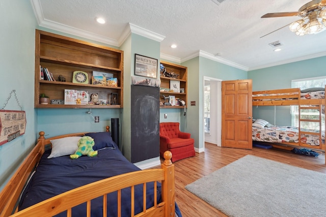 bedroom with visible vents, a textured ceiling, crown molding, and light wood-style floors