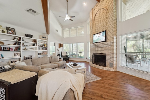 living area with visible vents, high vaulted ceiling, a ceiling fan, wood finished floors, and a brick fireplace