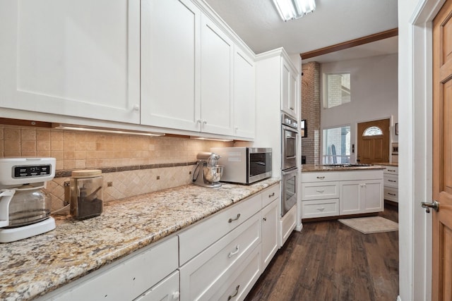 kitchen with light stone counters, dark wood finished floors, white cabinetry, appliances with stainless steel finishes, and decorative backsplash