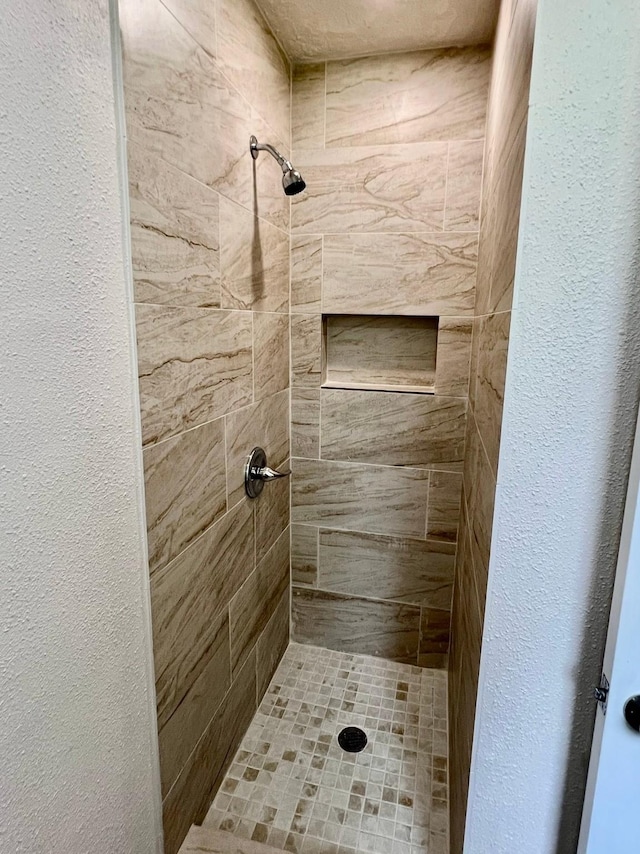 bathroom with a textured wall and a tile shower