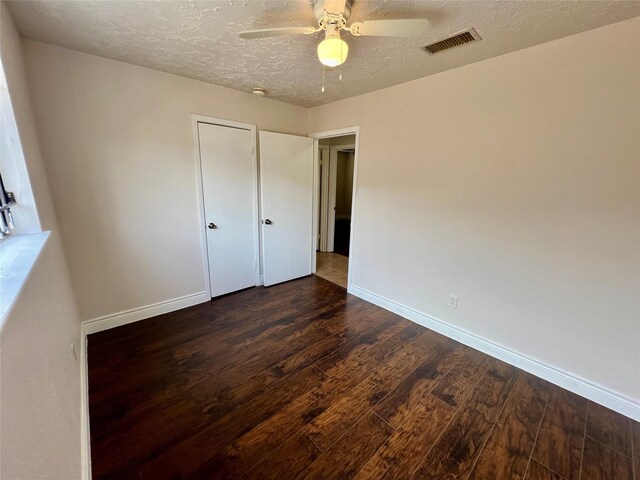 unfurnished bedroom with visible vents, a textured ceiling, dark wood-style floors, baseboards, and ceiling fan