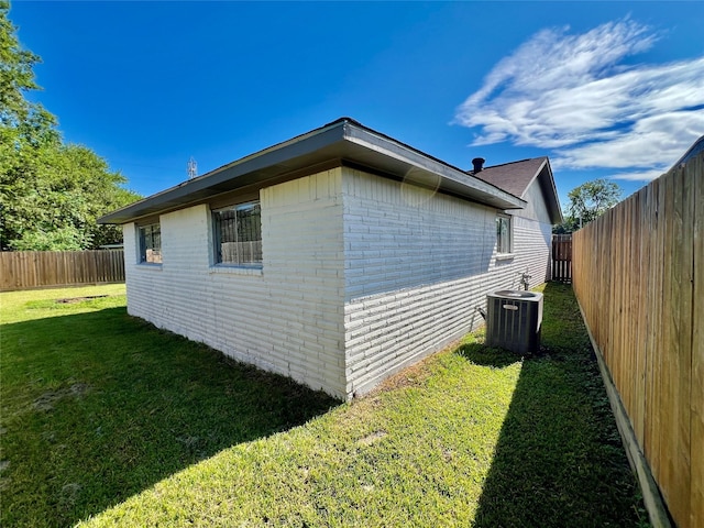 view of property exterior with a yard, brick siding, central AC unit, and a fenced backyard