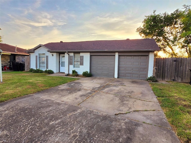 ranch-style home with a shingled roof, fence, concrete driveway, a garage, and a yard