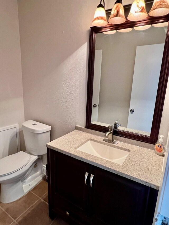 bathroom featuring tile patterned floors, toilet, vanity, and a textured wall