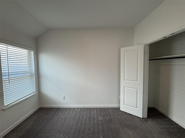 unfurnished bedroom with dark colored carpet, a closet, baseboards, and lofted ceiling