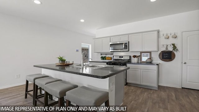 kitchen featuring a sink, a kitchen breakfast bar, dark countertops, dark wood finished floors, and stainless steel appliances