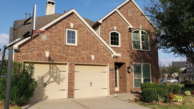 view of front of house featuring a chimney, brick siding, an attached garage, and driveway