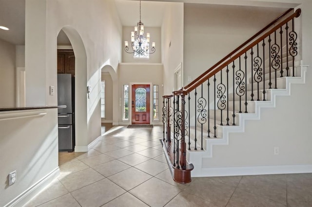 foyer entrance featuring arched walkways, baseboards, light tile patterned floors, a chandelier, and a high ceiling