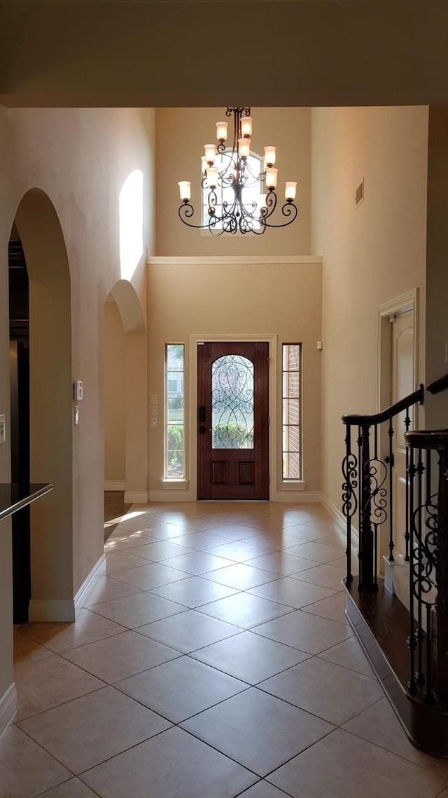entrance foyer with a towering ceiling, light tile patterned floors, arched walkways, a chandelier, and baseboards