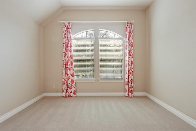 carpeted spare room featuring healthy amount of natural light, vaulted ceiling, and baseboards