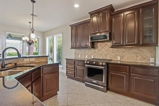kitchen featuring appliances with stainless steel finishes, a sink, dark stone counters, backsplash, and hanging light fixtures