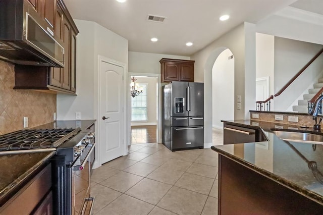 kitchen featuring appliances with stainless steel finishes, a sink, dark stone countertops, arched walkways, and tasteful backsplash