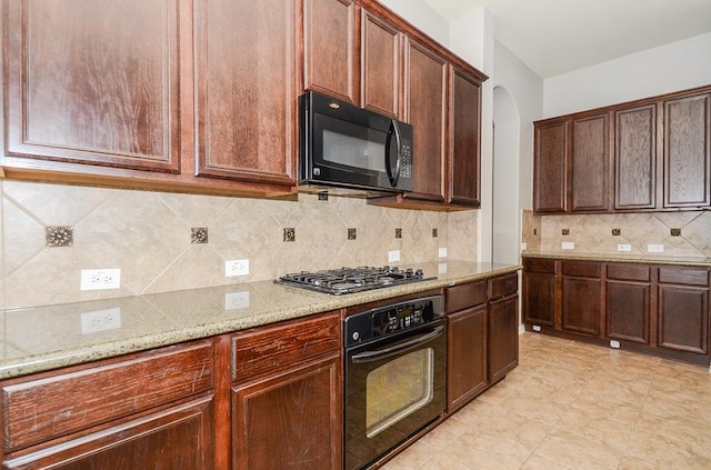 kitchen with light stone counters, decorative backsplash, arched walkways, and black appliances