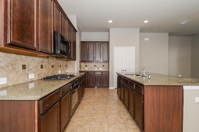 kitchen featuring tasteful backsplash, light stone countertops, a center island with sink, black appliances, and a sink