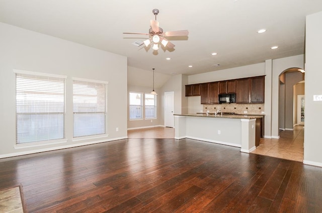 unfurnished living room with hardwood / wood-style floors, arched walkways, baseboards, ceiling fan, and vaulted ceiling