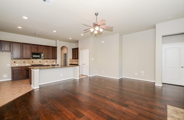 kitchen with wood finished floors, arched walkways, ceiling fan, black microwave, and tasteful backsplash