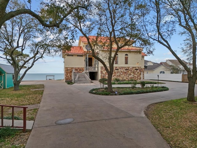 mediterranean / spanish home with stucco siding, stone siding, curved driveway, and a tiled roof