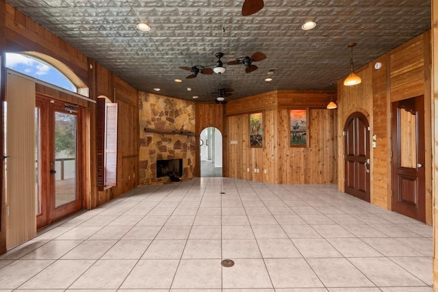 unfurnished living room featuring a fireplace, arched walkways, wood walls, and ceiling fan