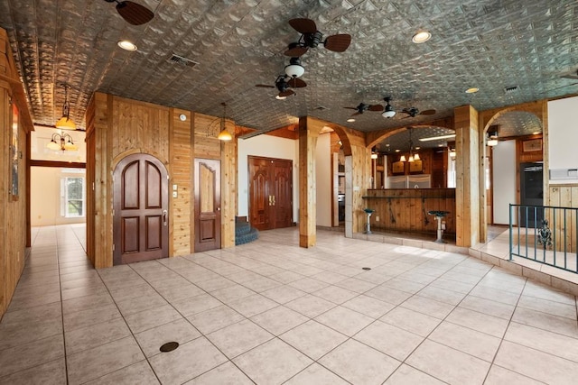 interior space featuring tile patterned flooring, visible vents, wood walls, arched walkways, and a ceiling fan