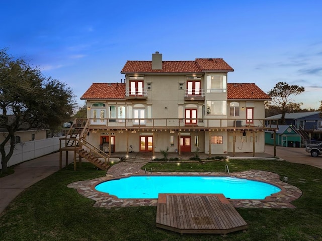 back of property at dusk featuring stucco siding, a tile roof, french doors, a balcony, and a chimney