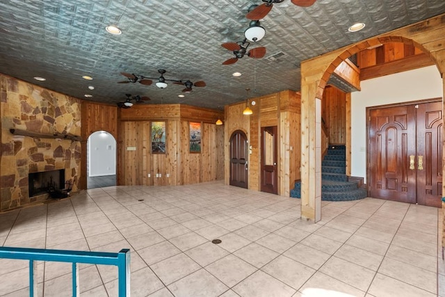 unfurnished living room with visible vents, wooden walls, stairway, arched walkways, and a ceiling fan