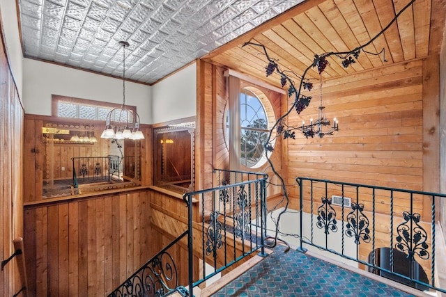 hall featuring wood ceiling, an upstairs landing, wood walls, and a chandelier