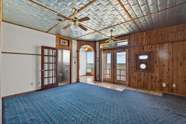 unfurnished room featuring carpet flooring, french doors, wood walls, and ceiling fan