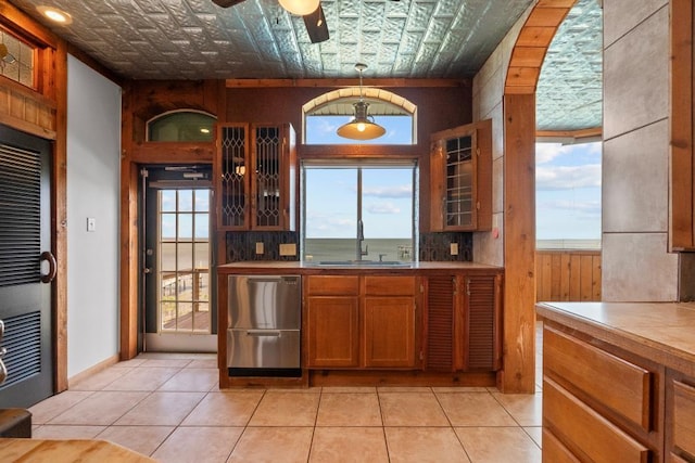 kitchen with a sink, an ornate ceiling, stainless steel dishwasher, brown cabinetry, and ceiling fan